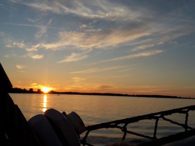 Ein Sonnenuntergang über dem Wasser. Am Horizont ist der Himmel orange. Am Himmel sind wenige Wolken und werden orange angestrahlt.
