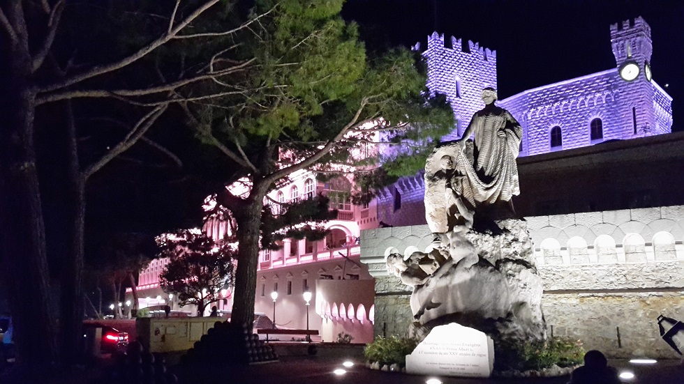Im Vordergund steht eine Statue, im Hintergrund wird der Grimaldi-Palast in pinkem und lila Licht angestrahlt.